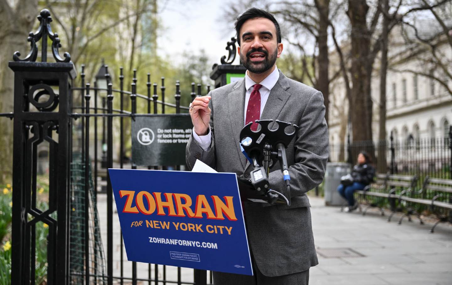 Zohran Mamdani stands in front of a plinth, passionately addressing a diverse group of supporters at a campaign rally.