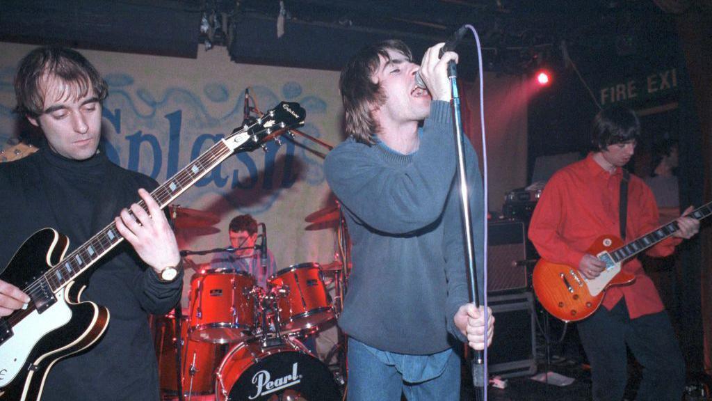 Younger Oasis performing energetically on stage at a small, packed venue during their early touring days.