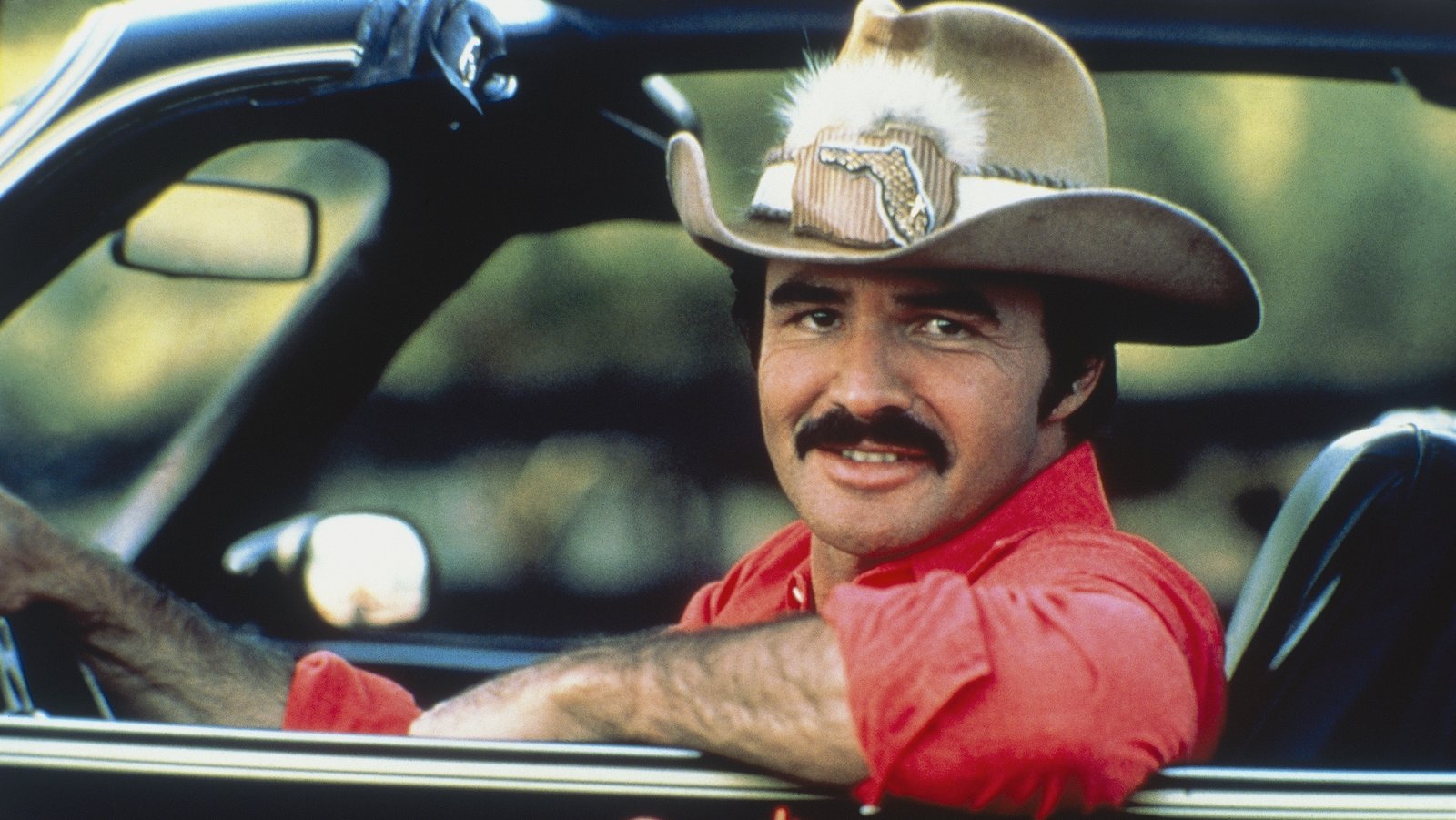 Burt Reynolds smiling behind the wheel of his iconic Pontiac Trans Am in Smokey and the Bandit.