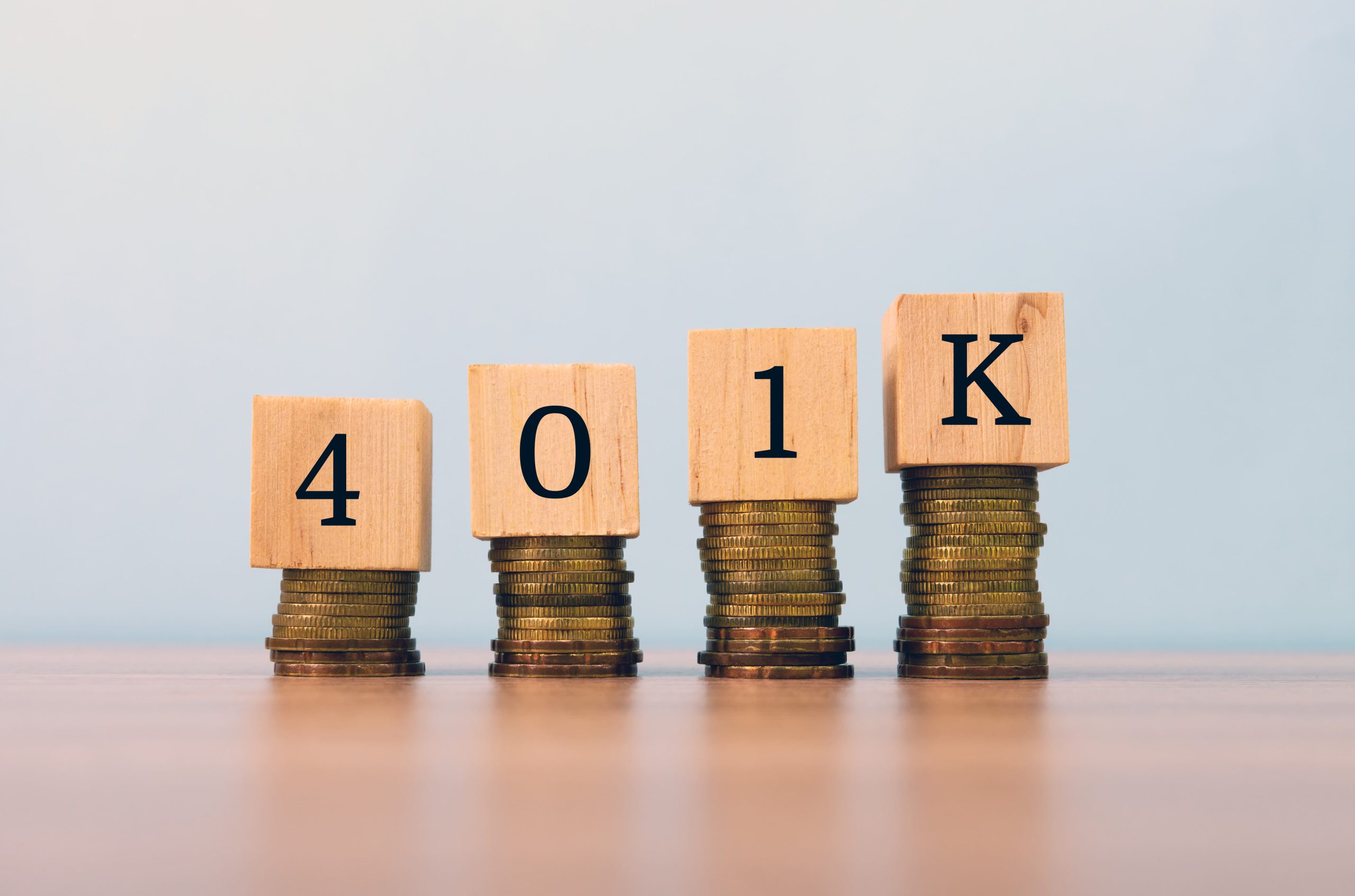 Wooden blocks spelling "401k" stacked on piles of coins, representing retirement savings growth.