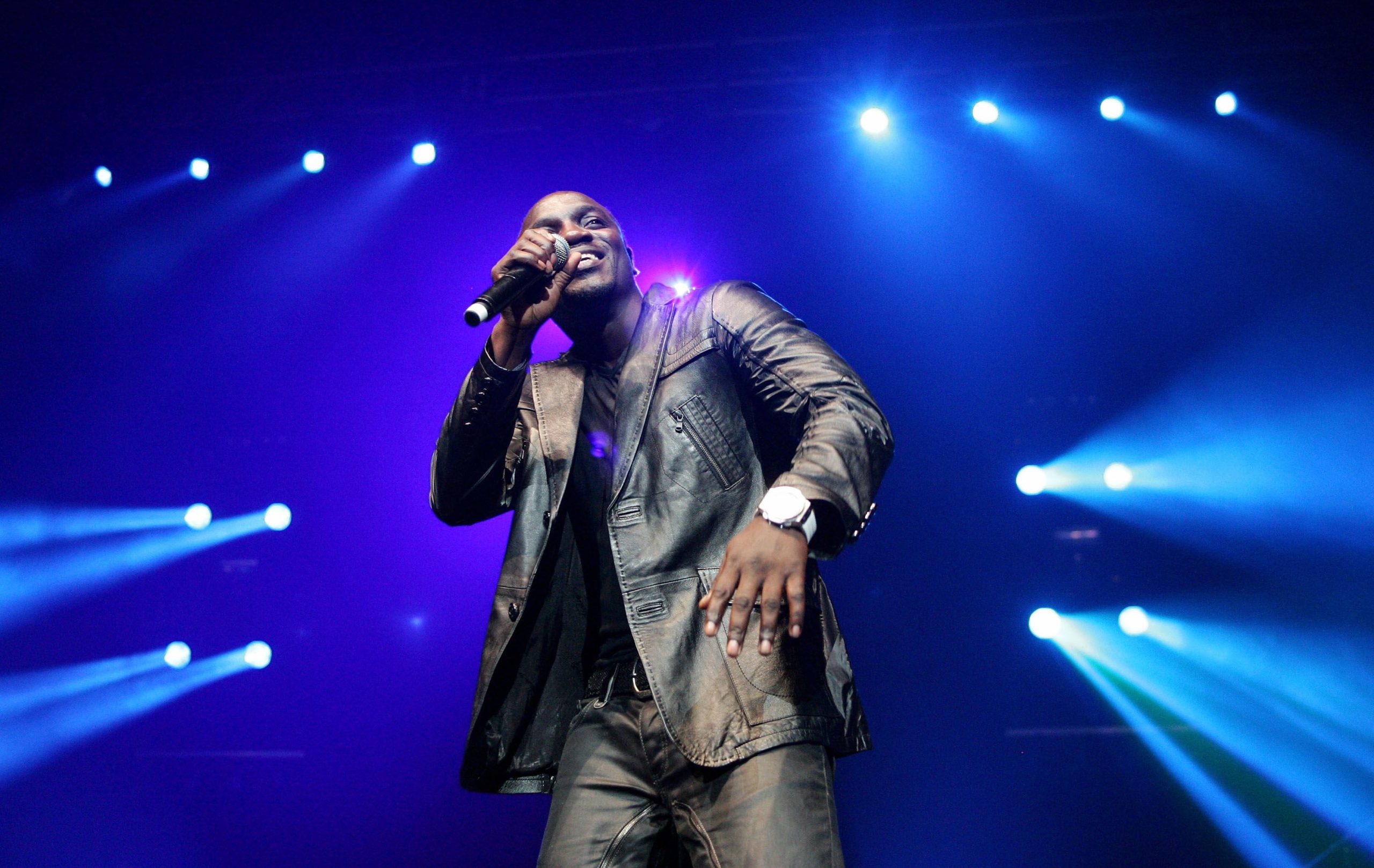 Akon performing live on stage under dramatic lighting during a concert.