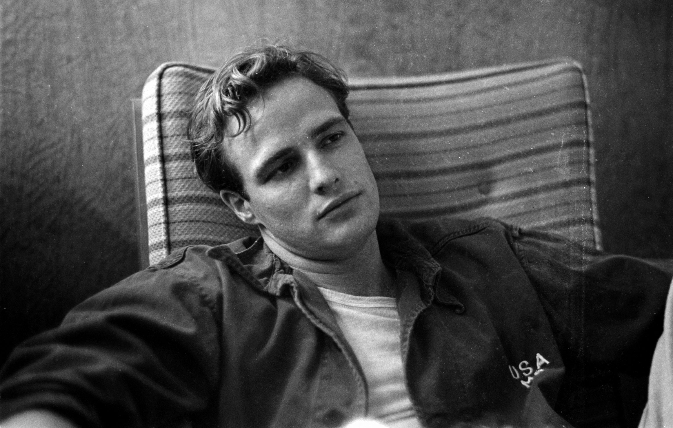 Young Marlon Brando sitting confidently in a chair wearing a USA jacket.