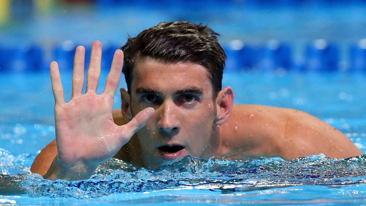 Michael Phelps in the pool holding up five fingers, celebrating a remarkable achievement.