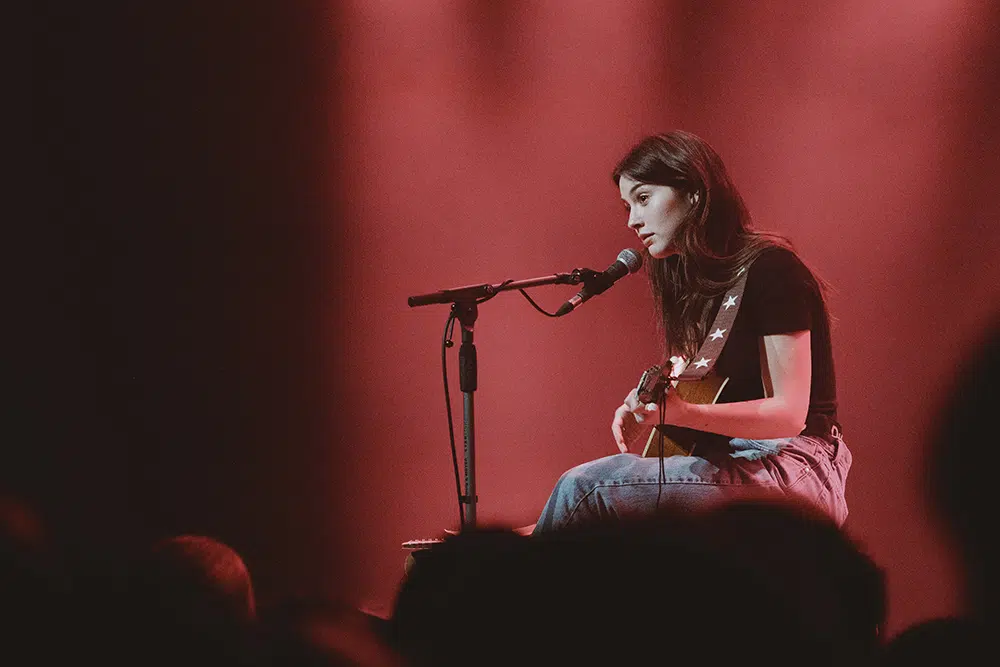 Gracie Abrams seated with her guitar, performing an intimate acoustic set in the UK venue.