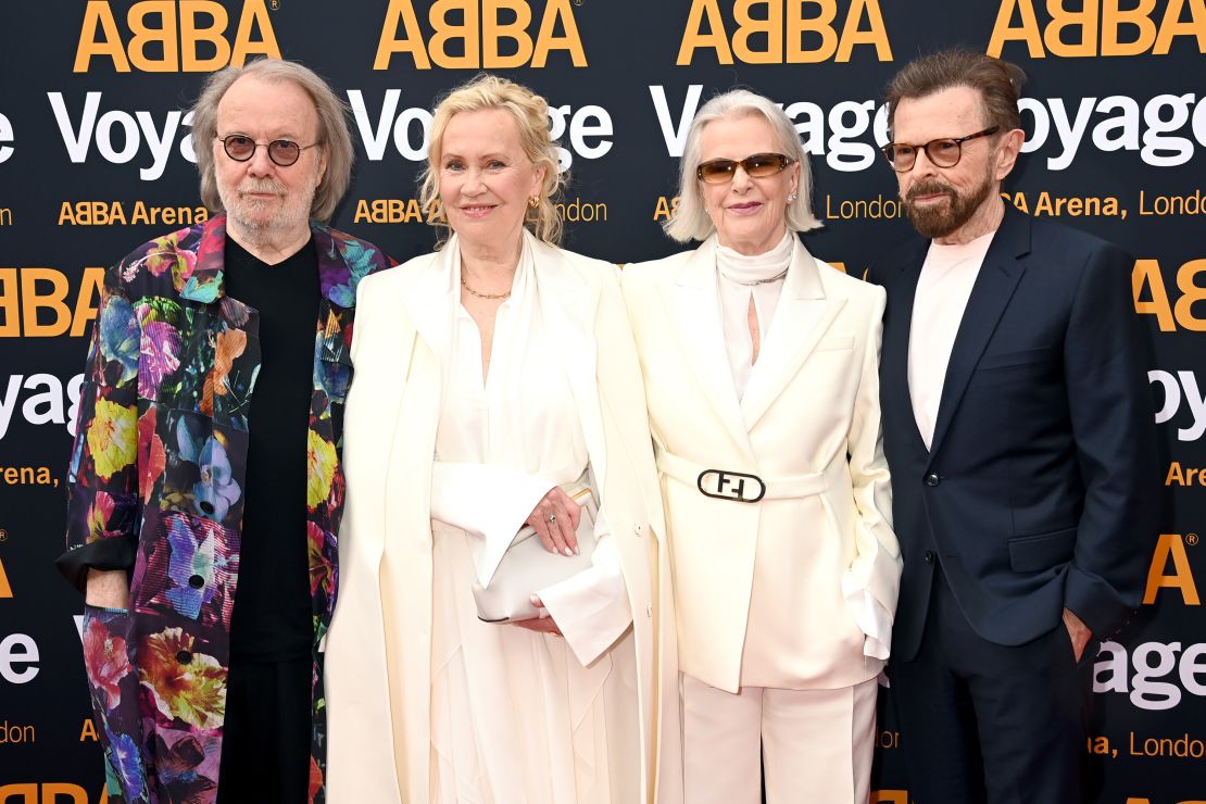 ABBA members posing together on the red carpet at the ABBA Voyage event, dressed in elegant attire with bright smiles and flashing cameras.