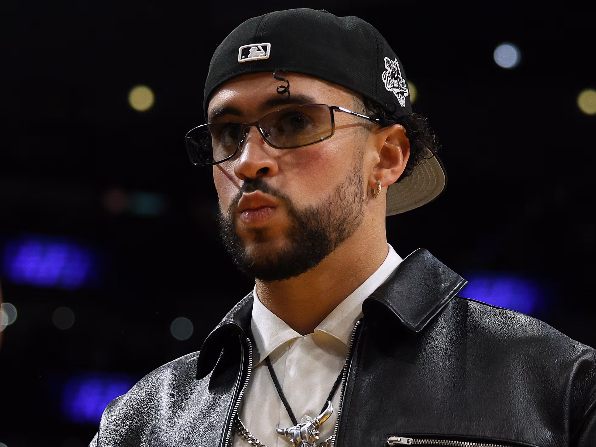 Bad Bunny attending an NBA game wearing a black leather jacket and a stylish hat.