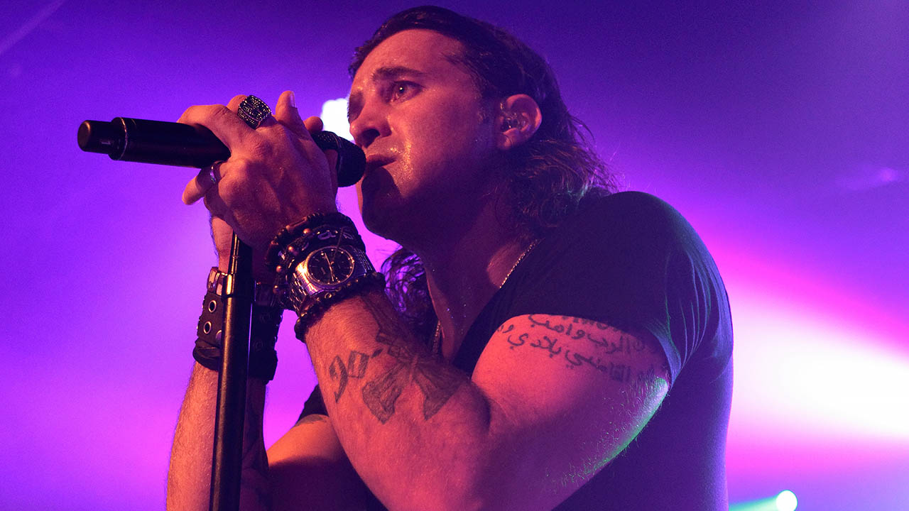 Scott Stapp performing on stage with dramatic neon purple lights glowing behind him, capturing the intensity of one of his anthemic songs.
