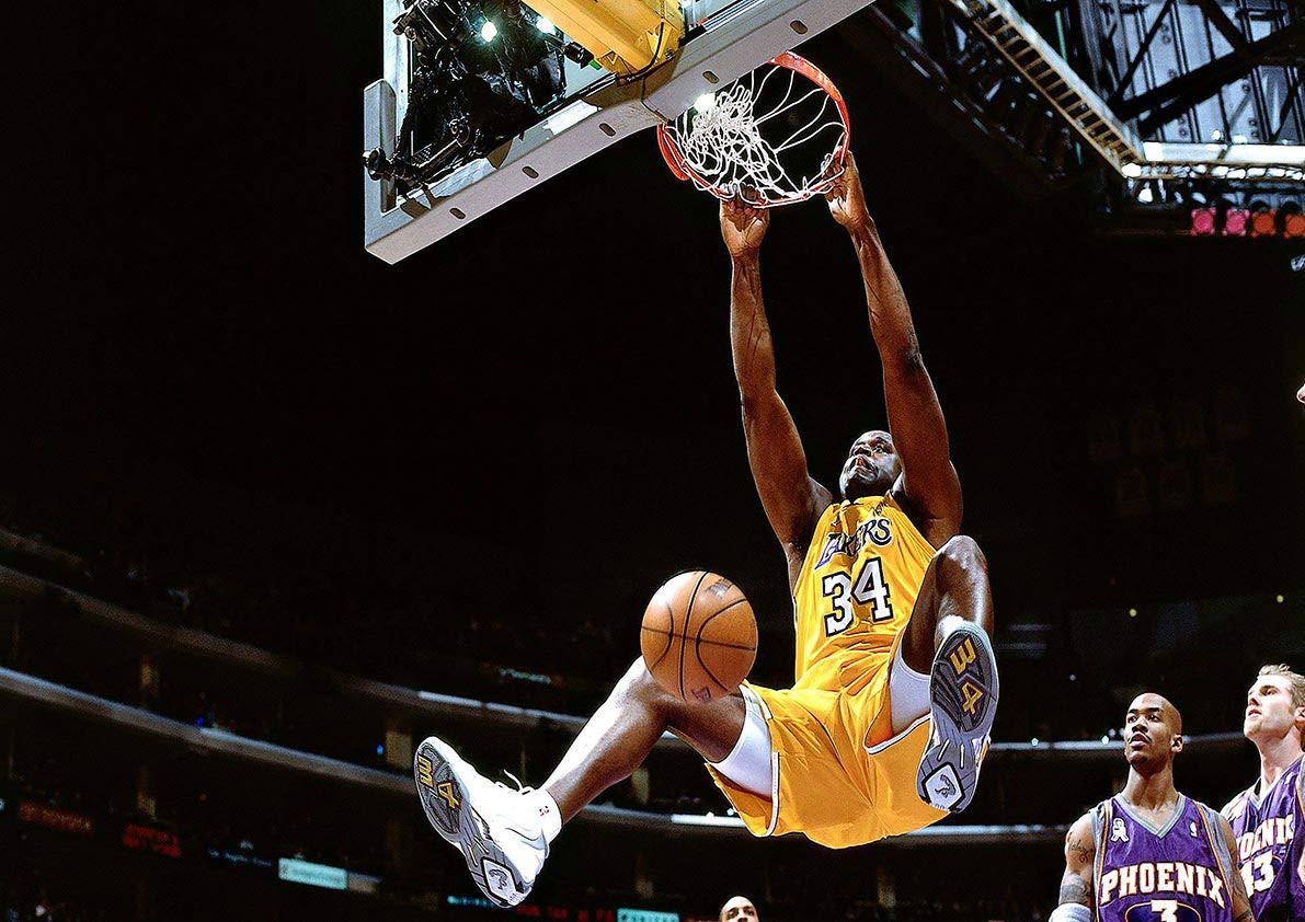 Shaquille O’Neal mid-air executing a powerful slam dunk in a Lakers jersey during an NBA game.