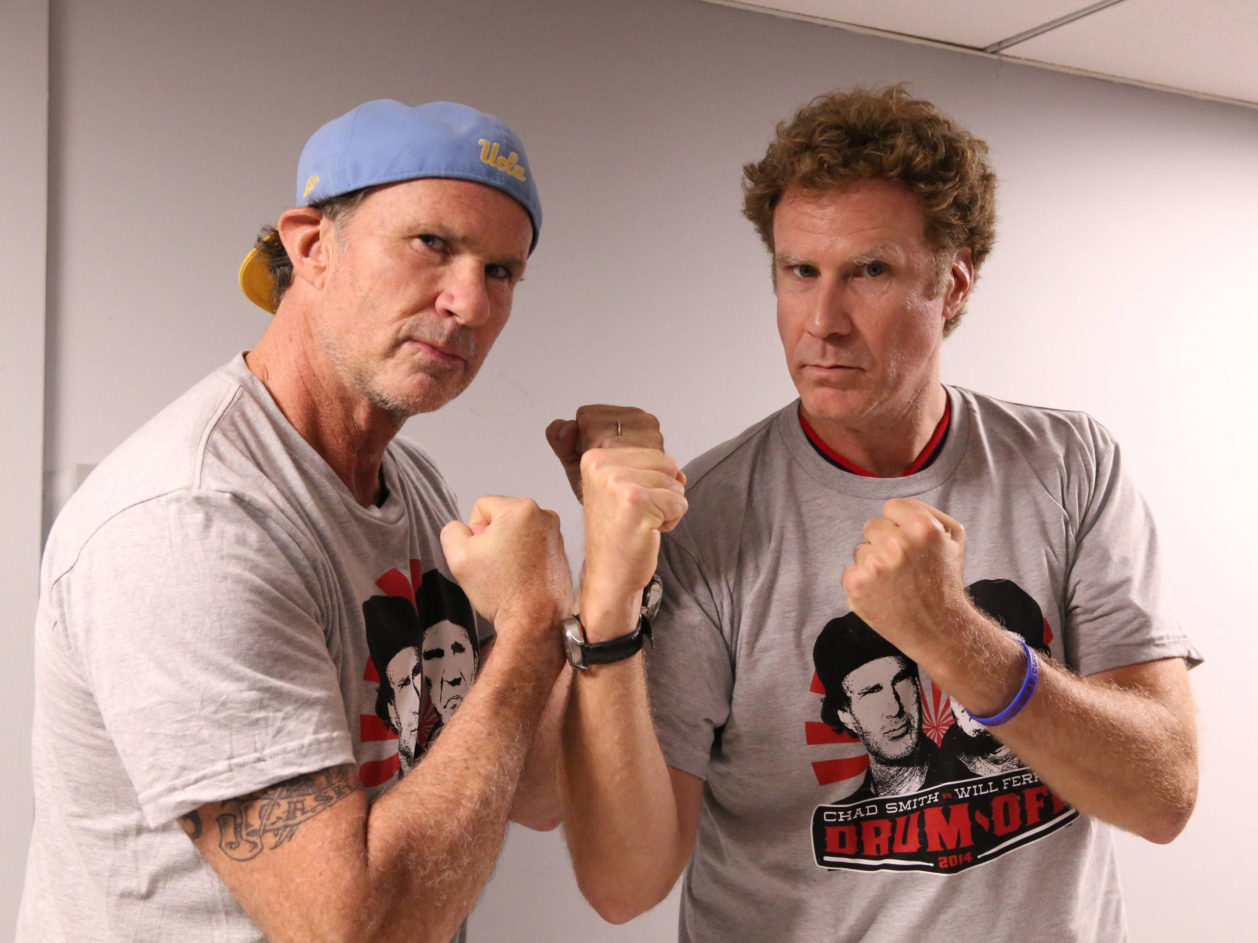 Chad Smith and Will Ferrell facing off with fists up, gearing up for their legendary drum battle.