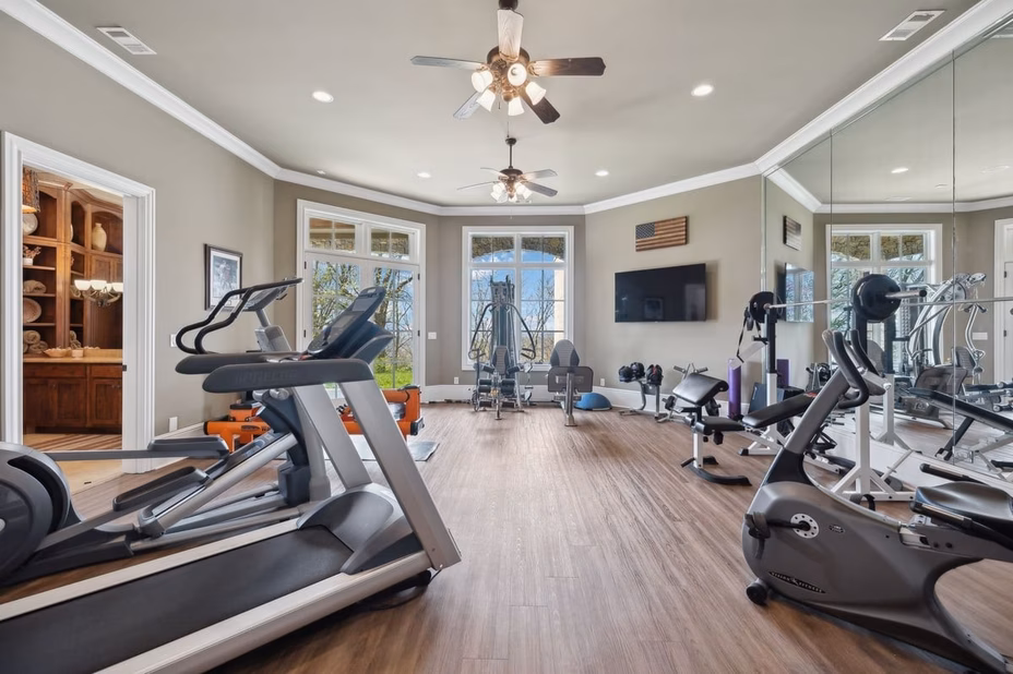 A well-equipped home gym with modern exercise machines, weights, and mirrors in Dave Ramsey’s Tennessee estate.