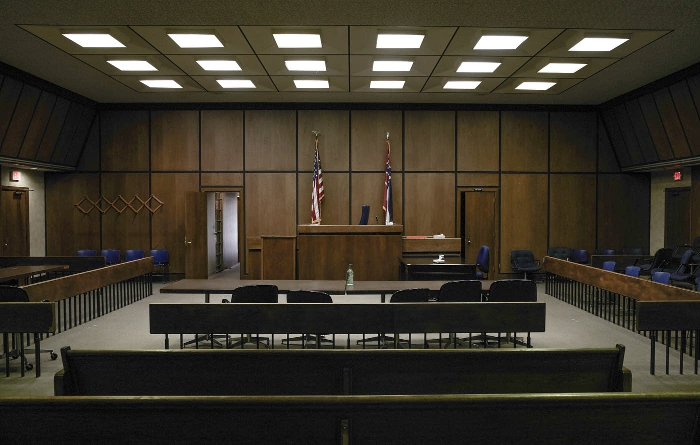 Empty courtroom with wood-paneled walls, judicial bench, and U.S. and state flags, symbolizing legal authority and public scrutiny.