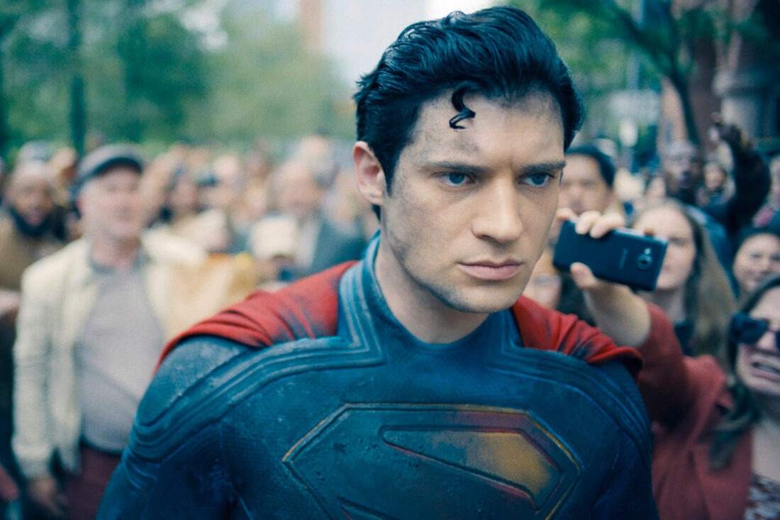 David Corenswet as Superman walking through a crowd with a serious expression, dressed in his iconic superhero suit.