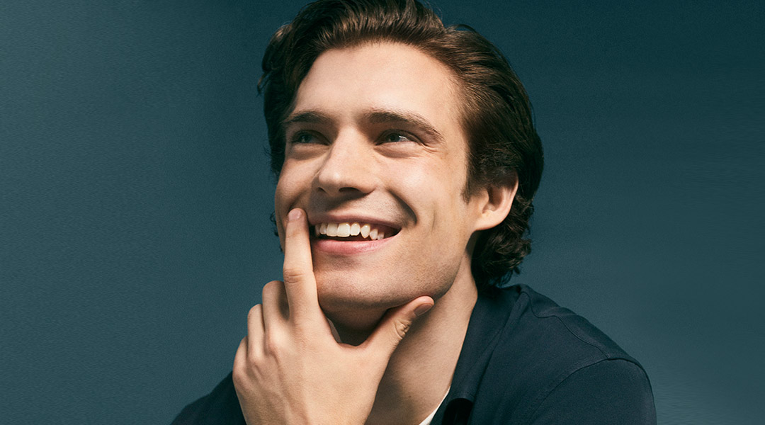 David Corenswet smiling thoughtfully with his hand resting on his chin, looking inquisitive.