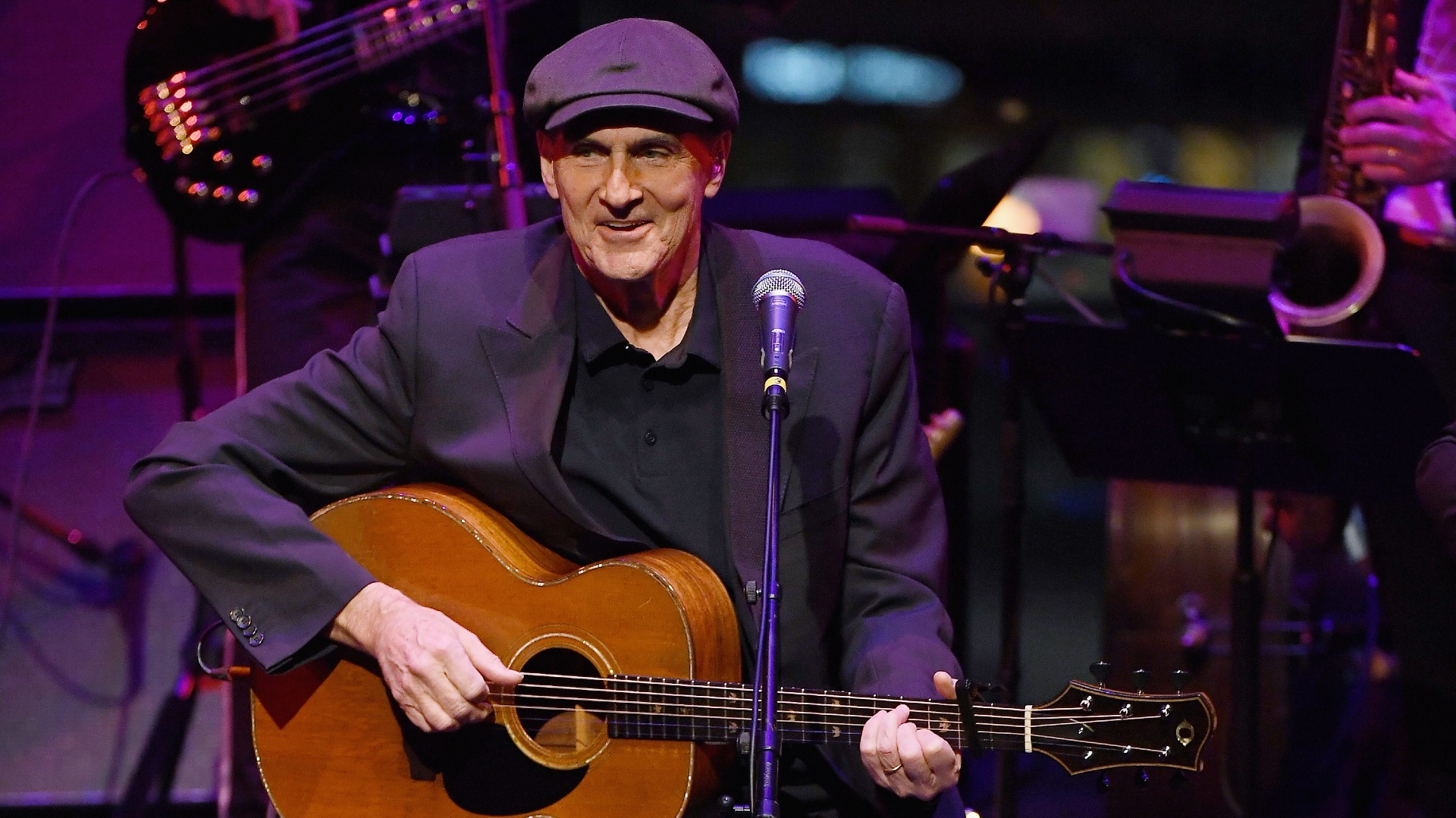 James Taylor performing live on stage with acoustic guitar during a 2024 concert tour.