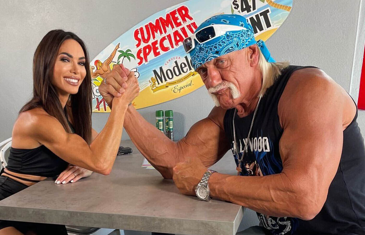 Hulk Hogan arm wrestling a female fan, both smiling and enjoying the playful competition.
