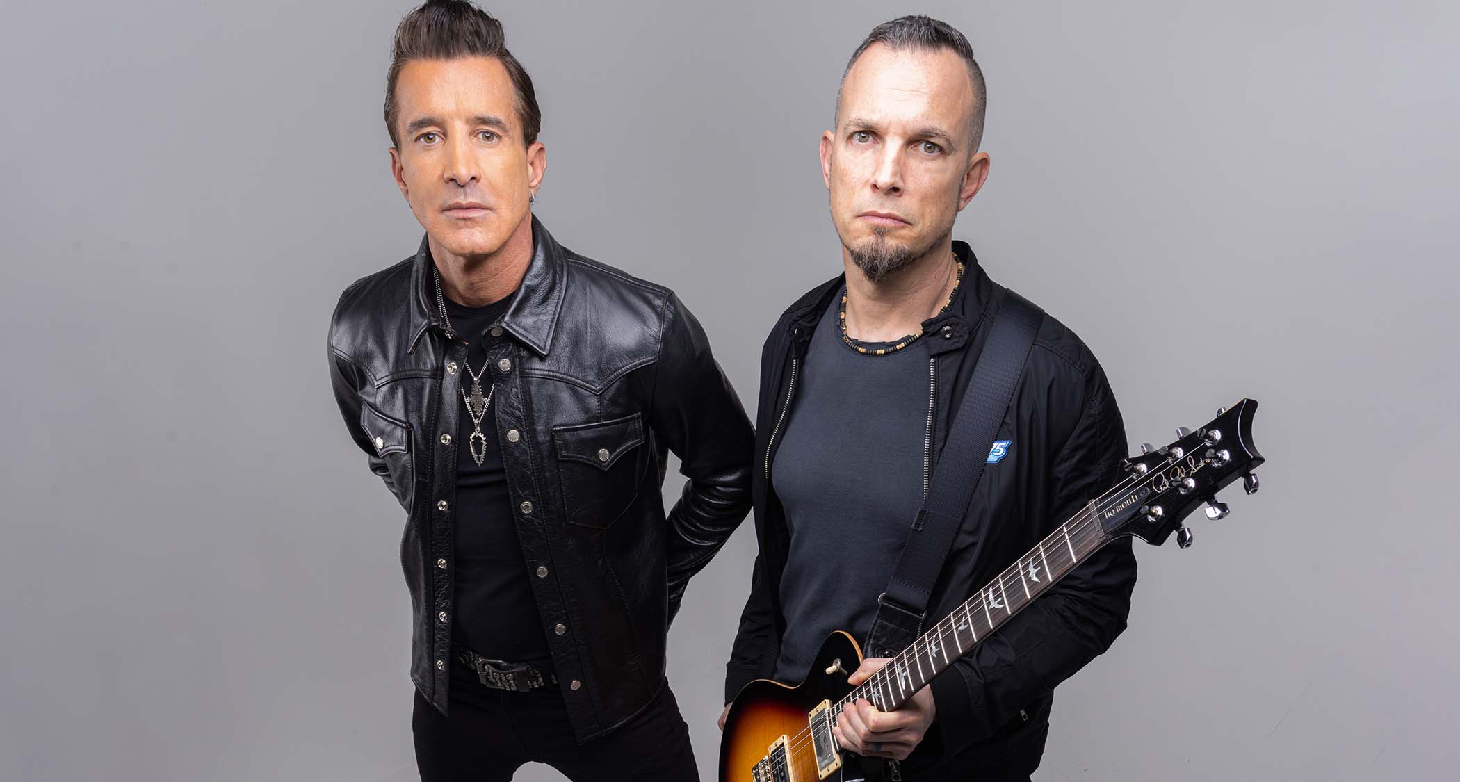 Mark Tremonti and Scott Stapp posing together during a professional photoshoot, both dressed in dark attire with serious expressions.