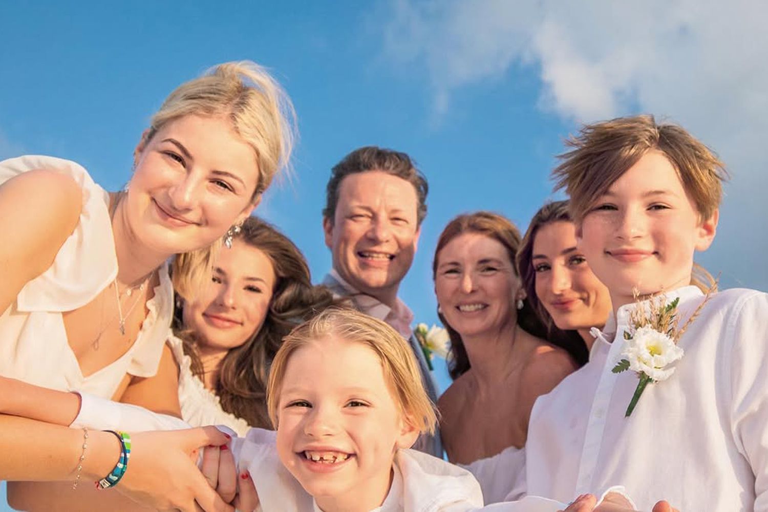 Jamie Oliver smiling warmly with his wife and their five children in a happy family portrait.