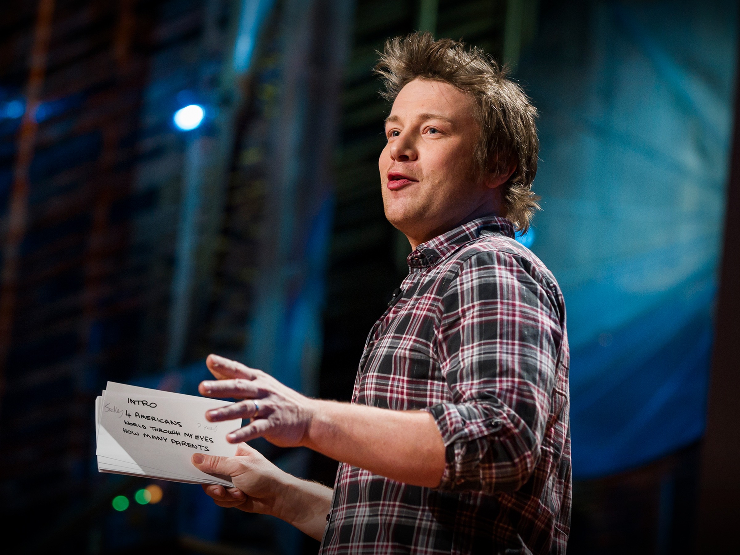 Young Jamie Oliver speaking passionately on stage during a 2010 food education talk.