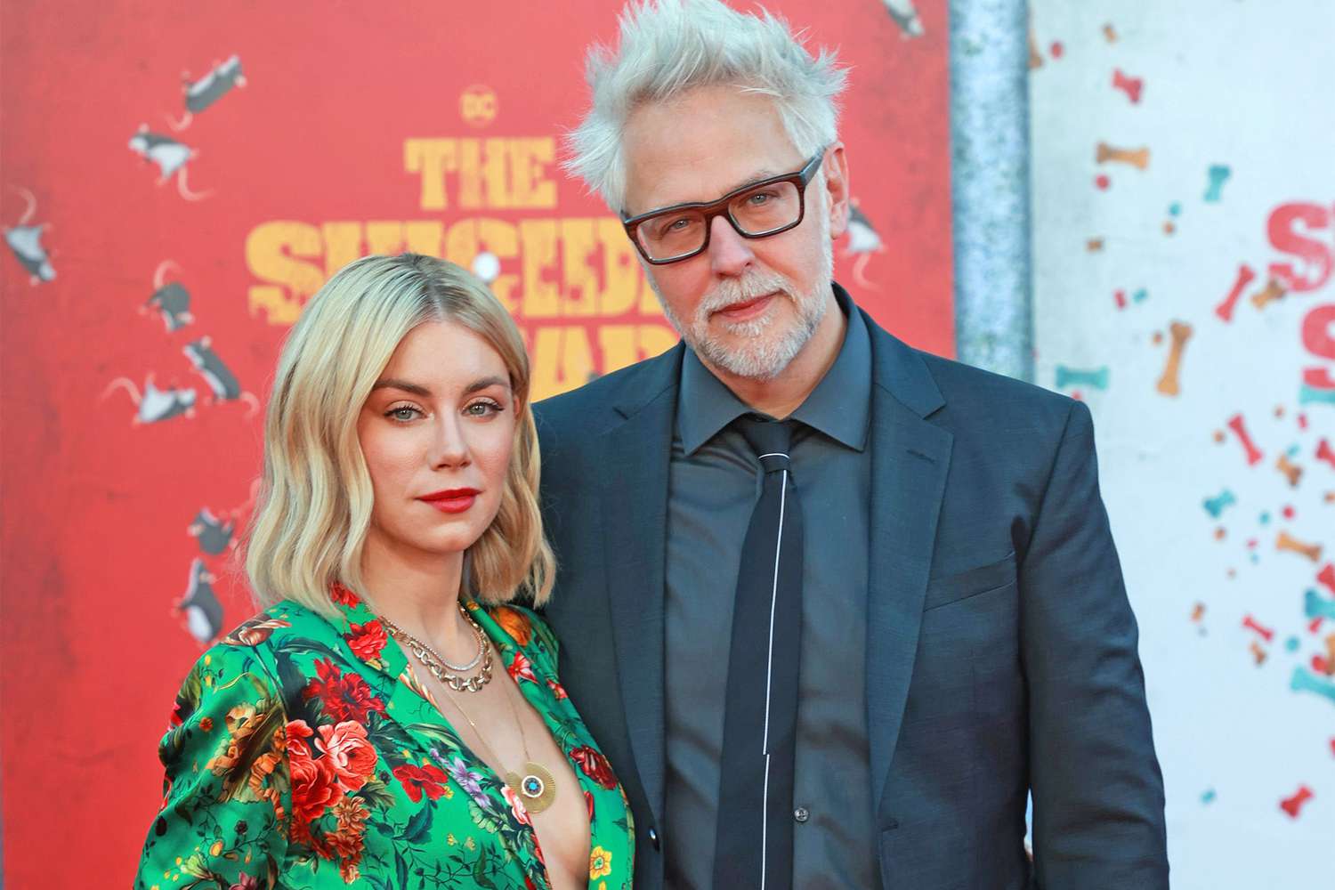 James Gunn and his wife smiling together on the red carpet.