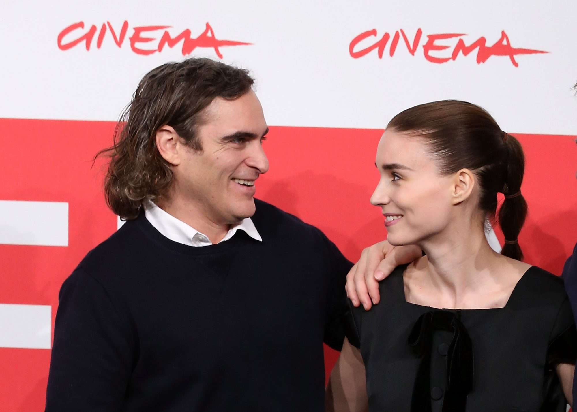 Joaquin Phoenix and his partner Rooney Mara smiling together at a public event, looking happy and close.