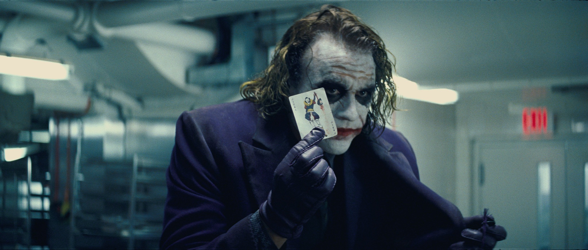 Heath Ledger as the Joker holding up a playing card with a sinister grin.