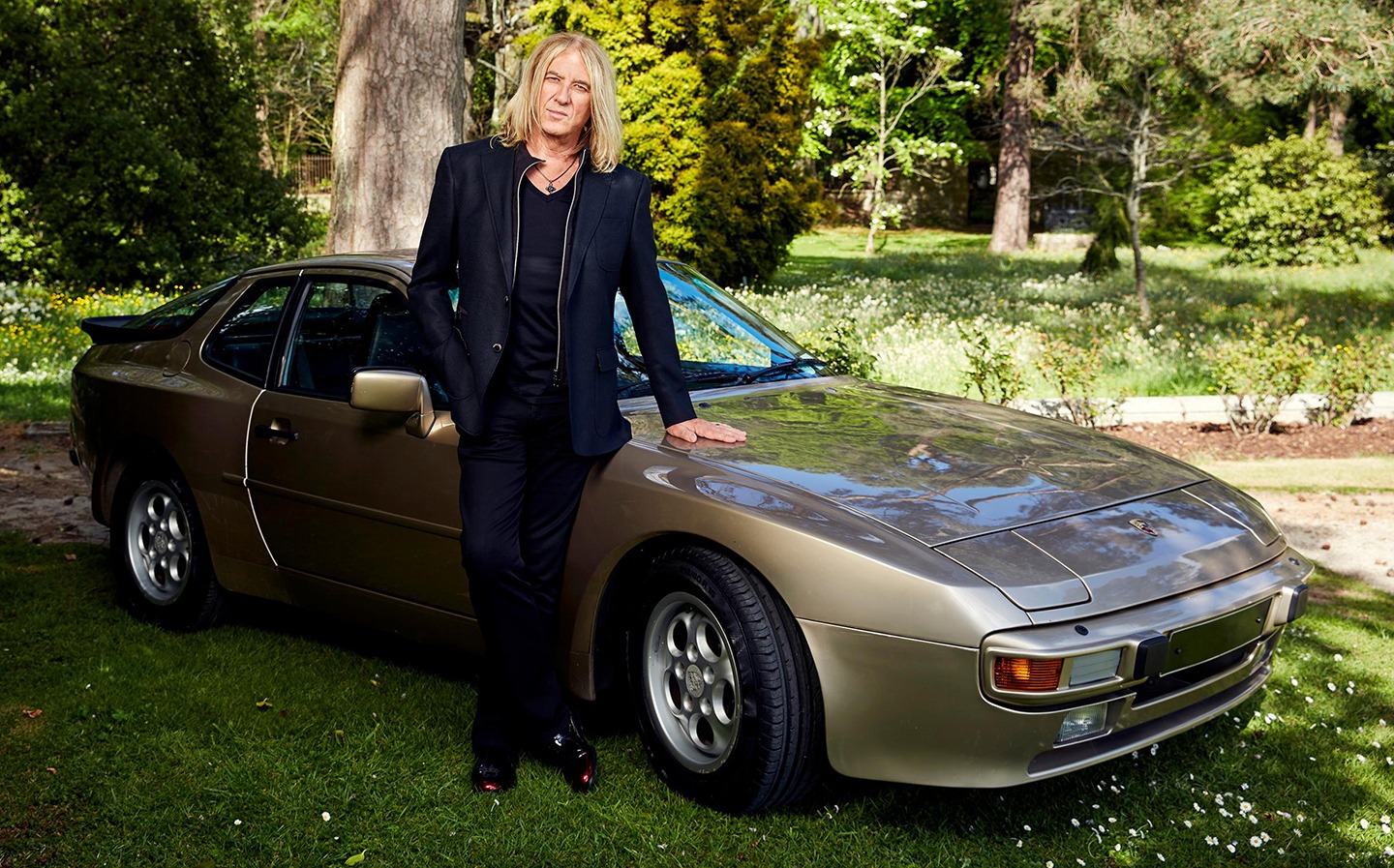 Joe Elliott standing proudly next to his classic Porsche car, showcasing his passion for vintage automobiles.