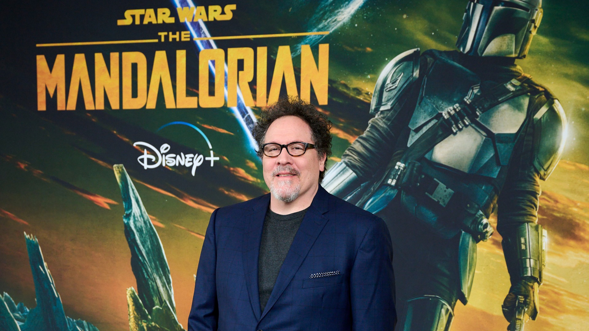 Jon Favreau smiling confidently on the red carpet at a film premiere.