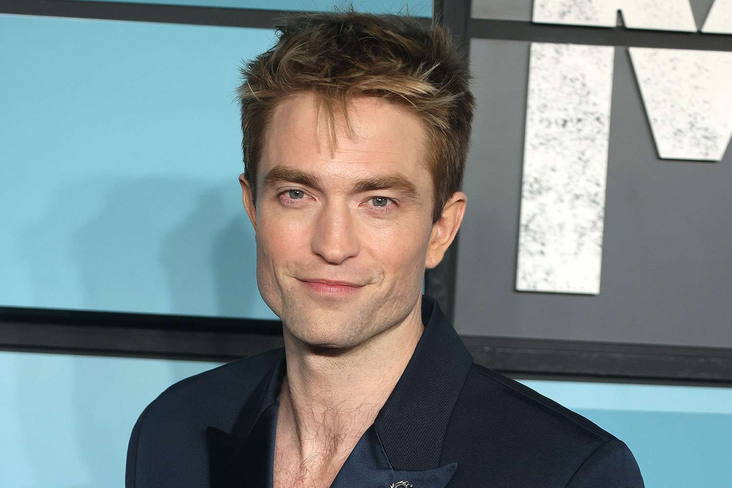 Robert Pattinson smiling warmly on the red carpet wearing a classic tuxedo.