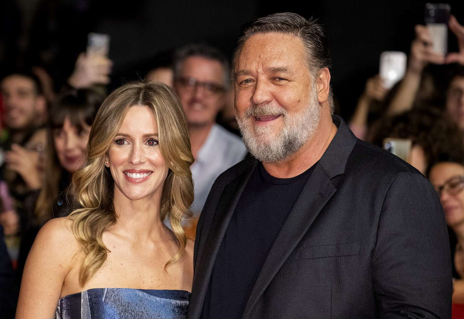 Russell Crowe smiling alongside his girlfriend, both dressed elegantly at a public event.