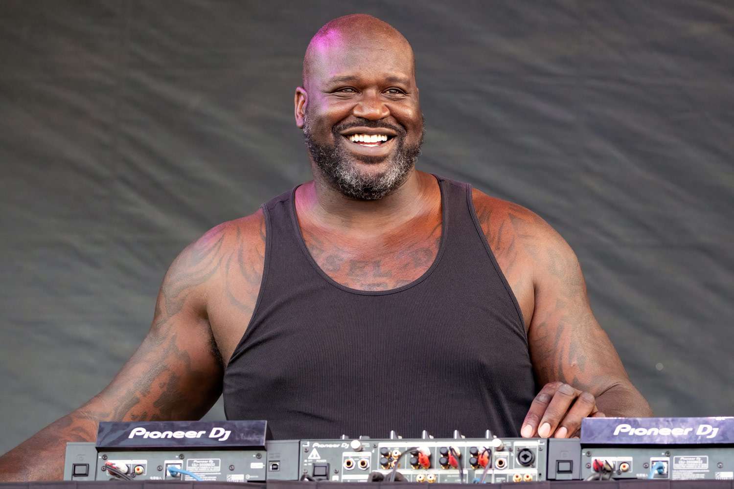 Shaquille O’Neal performing as a DJ at a music festival, hyping up the crowd from behind the decks.