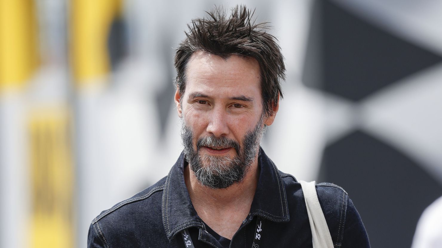 Keanu Reeves walking down the street smiling, dressed casually and appearing relaxed.