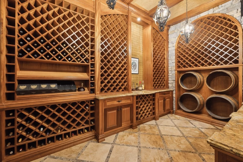 A climate-controlled wine cellar with wooden racks filled with bottles, ambient lighting, and stone flooring in Dave Ramsey’s Tennessee estate.