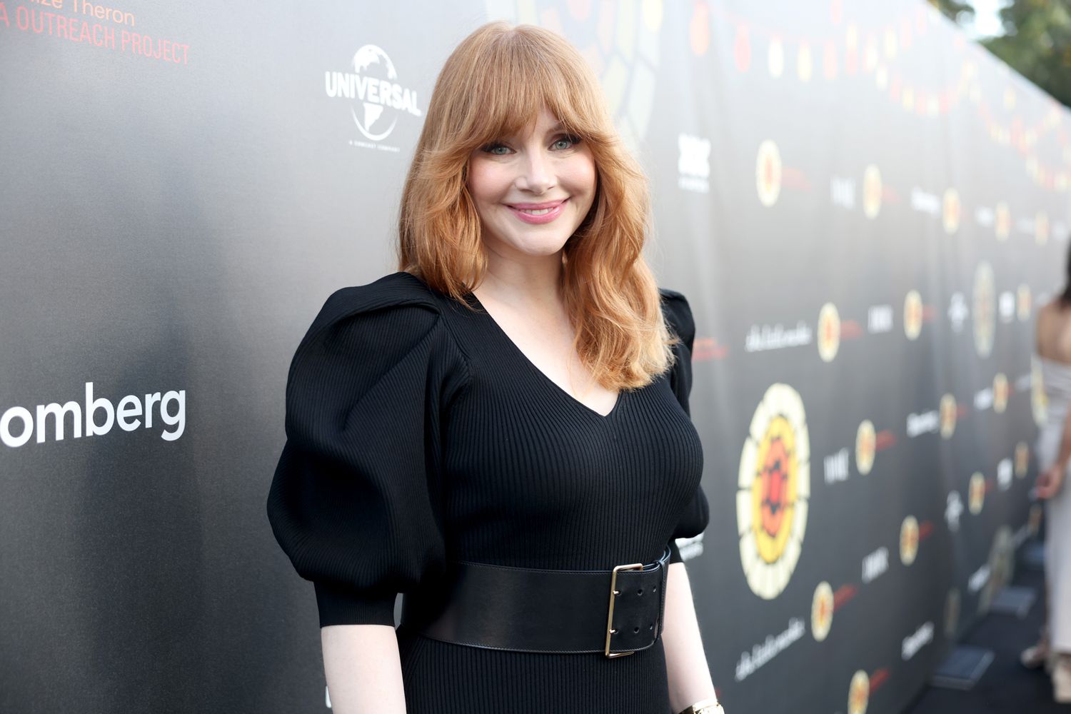 Bryce Dallas Howard wearing a sleek black dress on the red carpet, smiling for photographers.