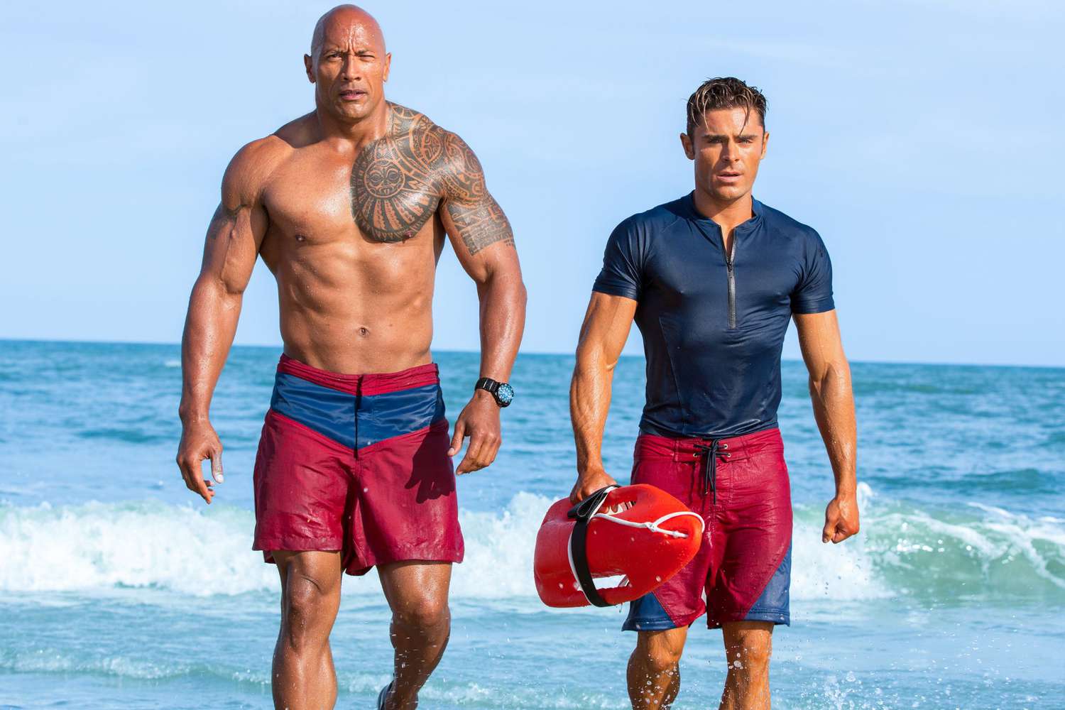 Zac Efron and Dwayne “The Rock” Johnson posing together on the set of Baywatch, both in lifeguard uniforms.