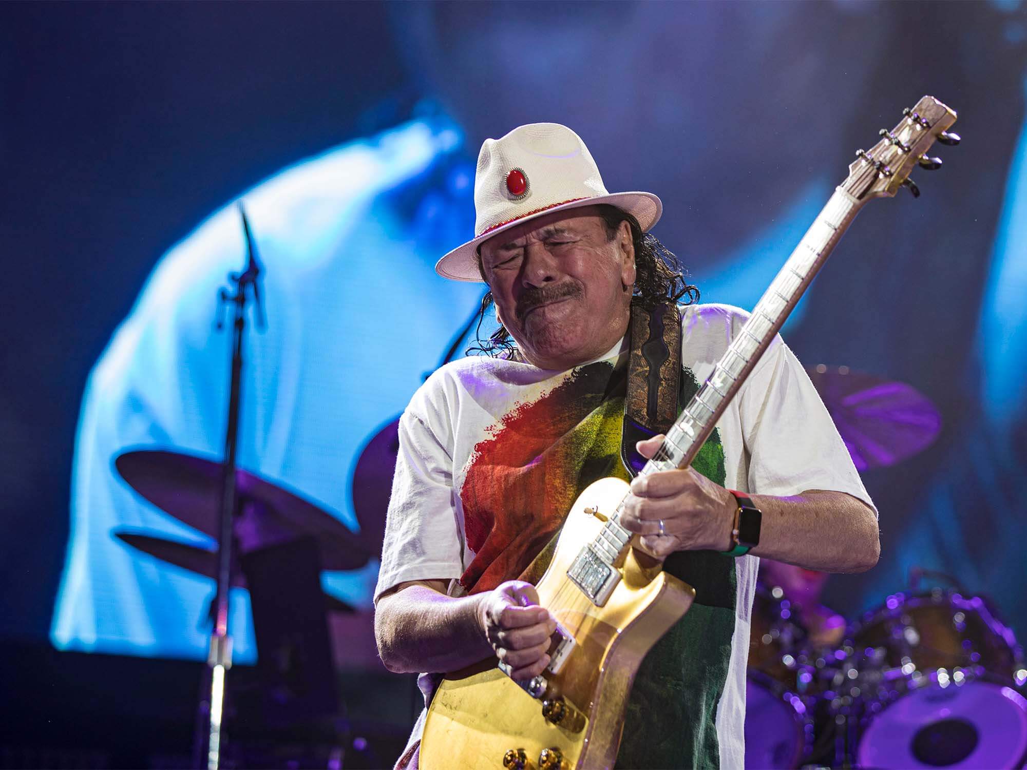 Carlos Santana intensely shredding a guitar solo on stage, eyes closed, fully immersed in the music.