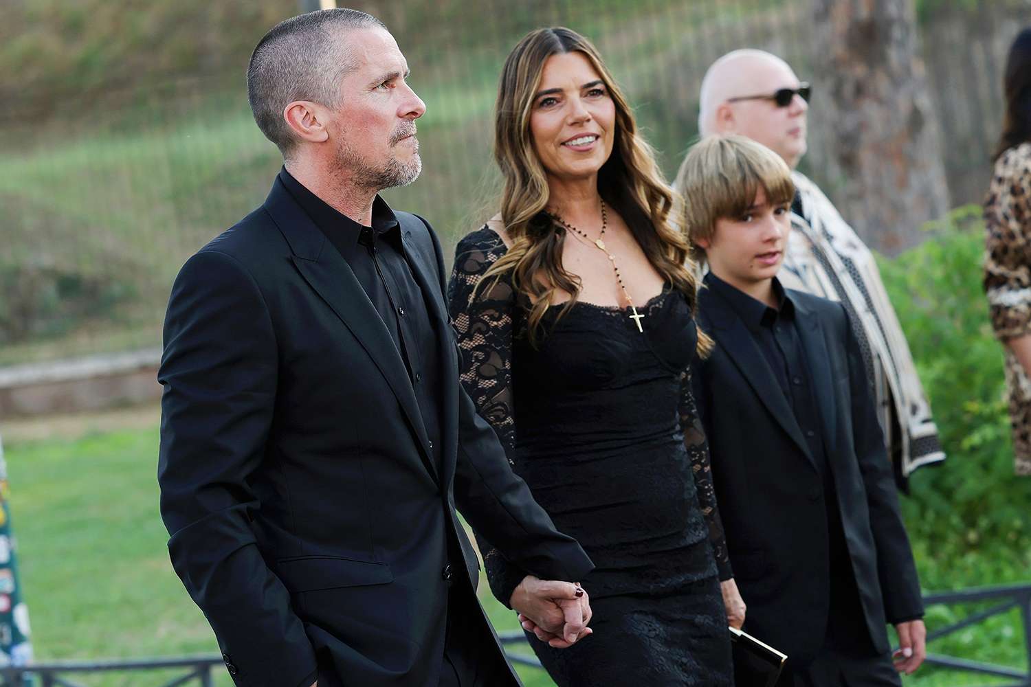 Christian Bale walking with his wife Sibi Blazic and their two children at a public event, all smiling and casually dressed.