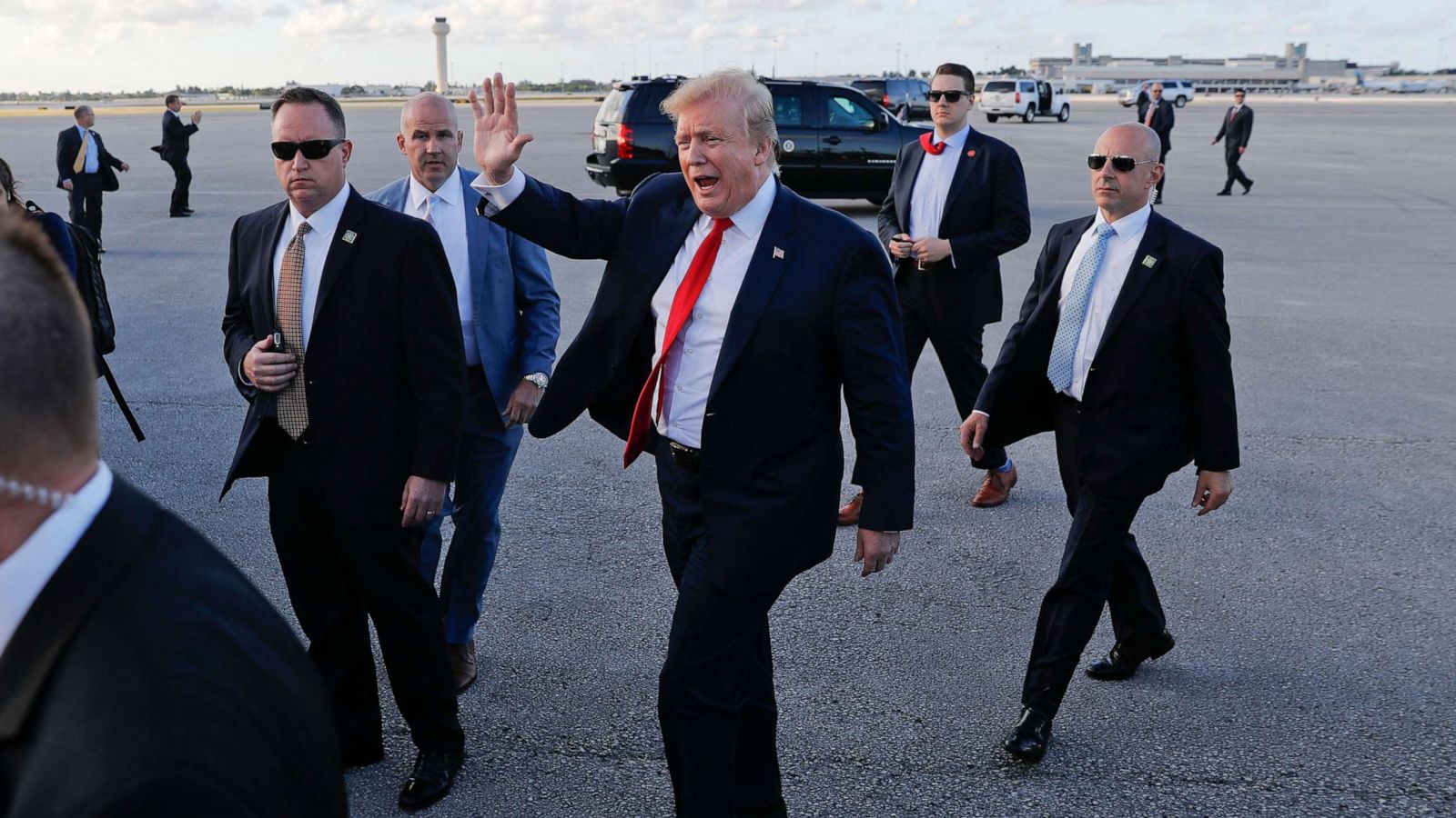 President Donald Trump waving while surrounded by Secret Service agents during a public appearance.