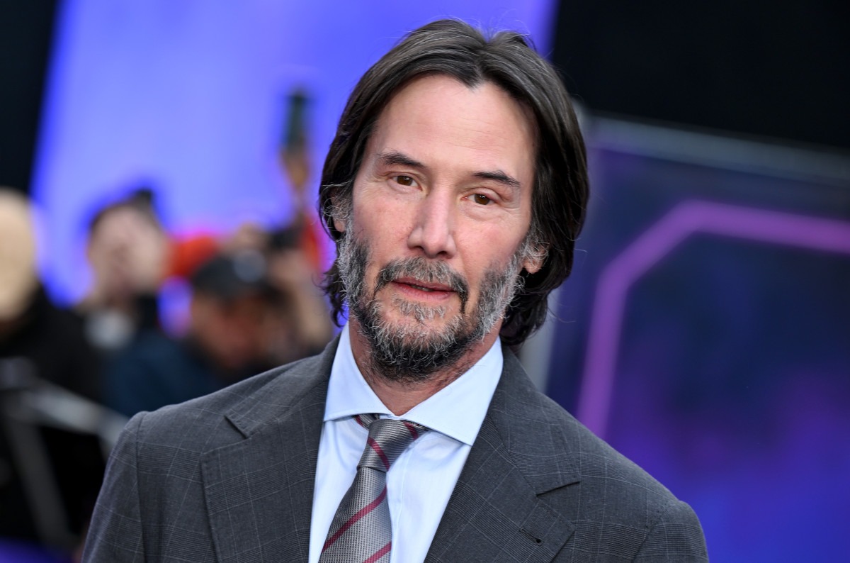 Keanu Reeves on the red carpet, looking directly at the camera in a classic grey suit.