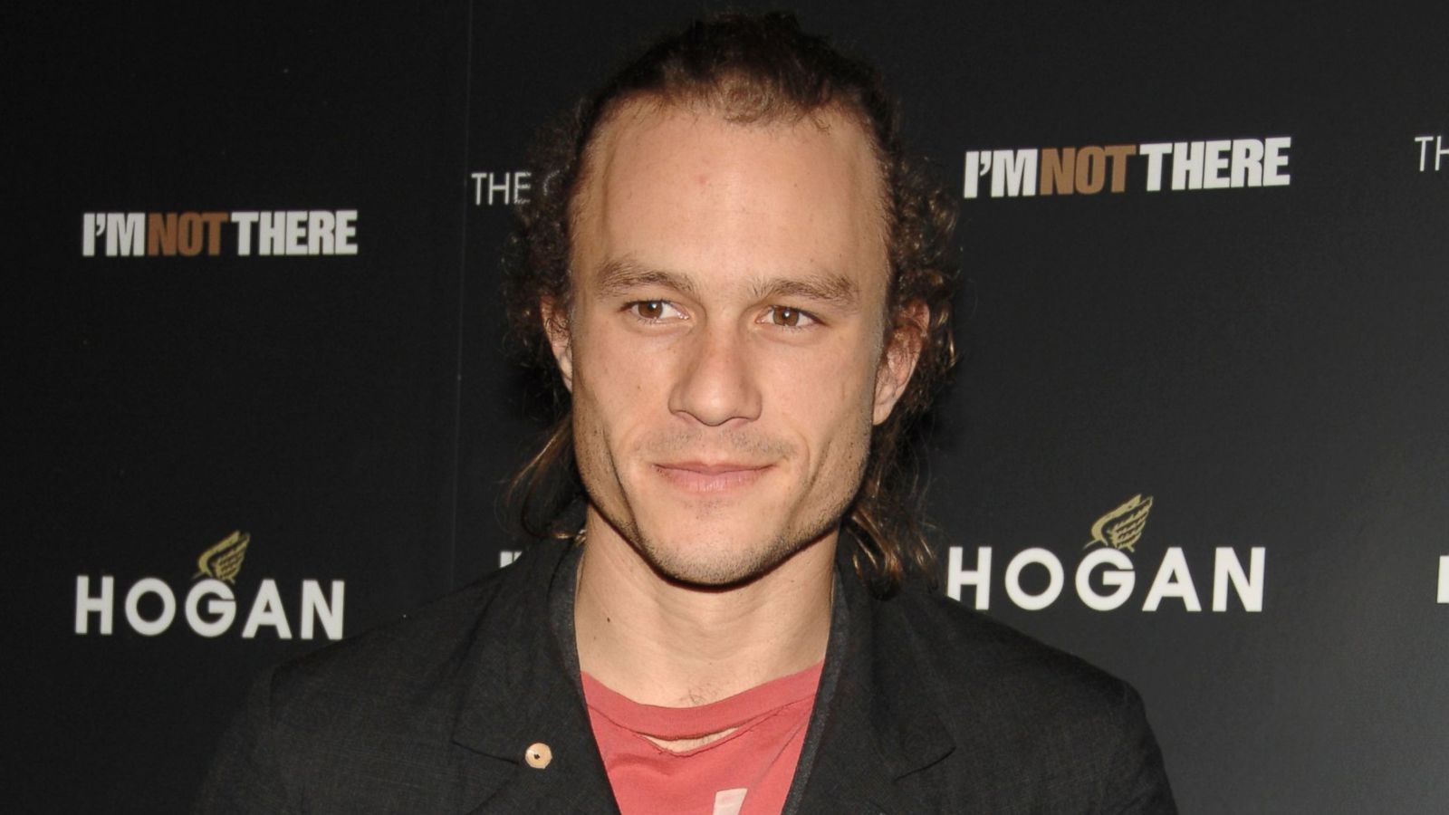 Heath Ledger smirking confidently on the red carpet in a tailored suit.