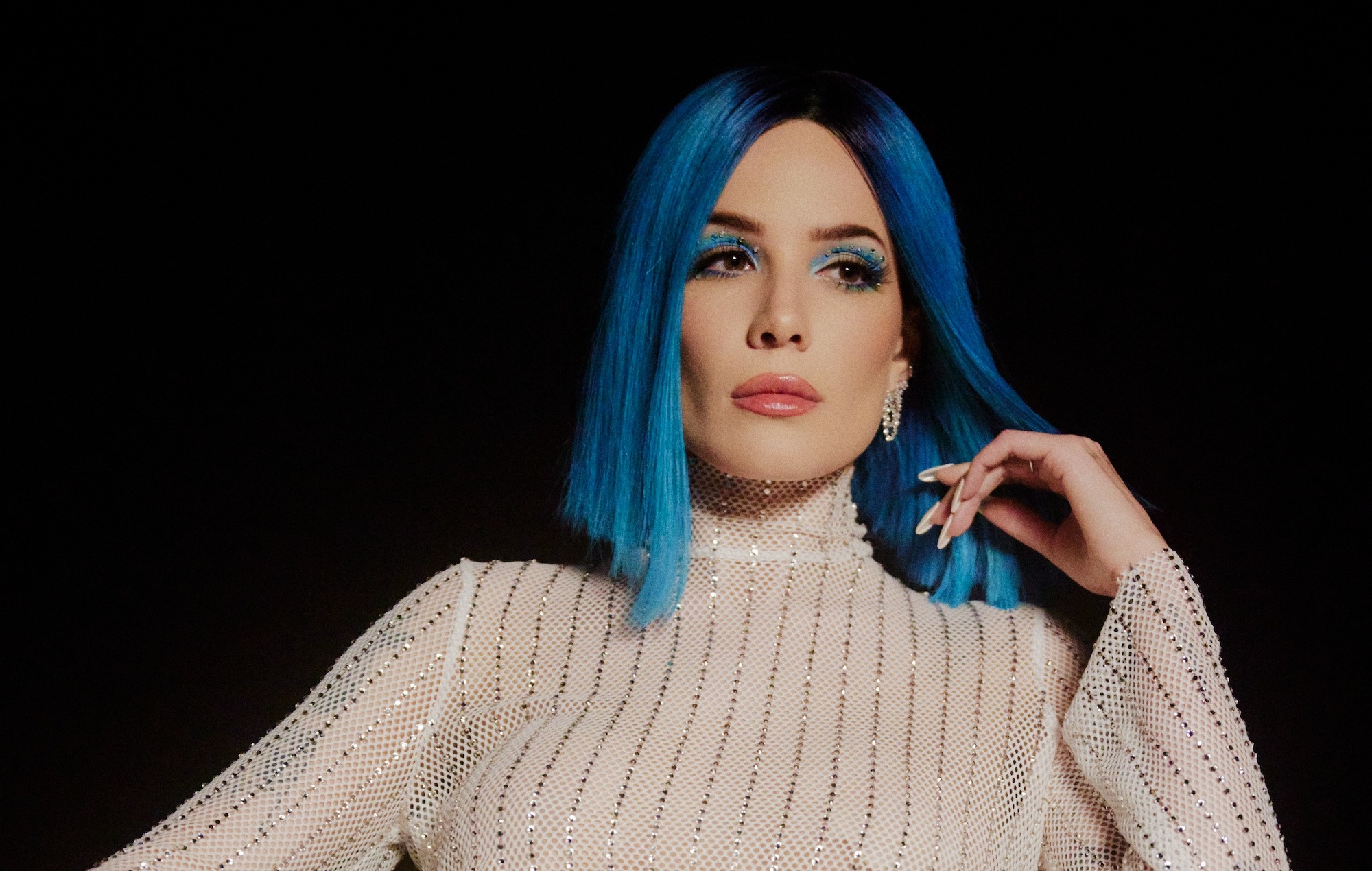 Halsey with vibrant blue hair posing confidently during a professional photoshoot against a neutral background.
