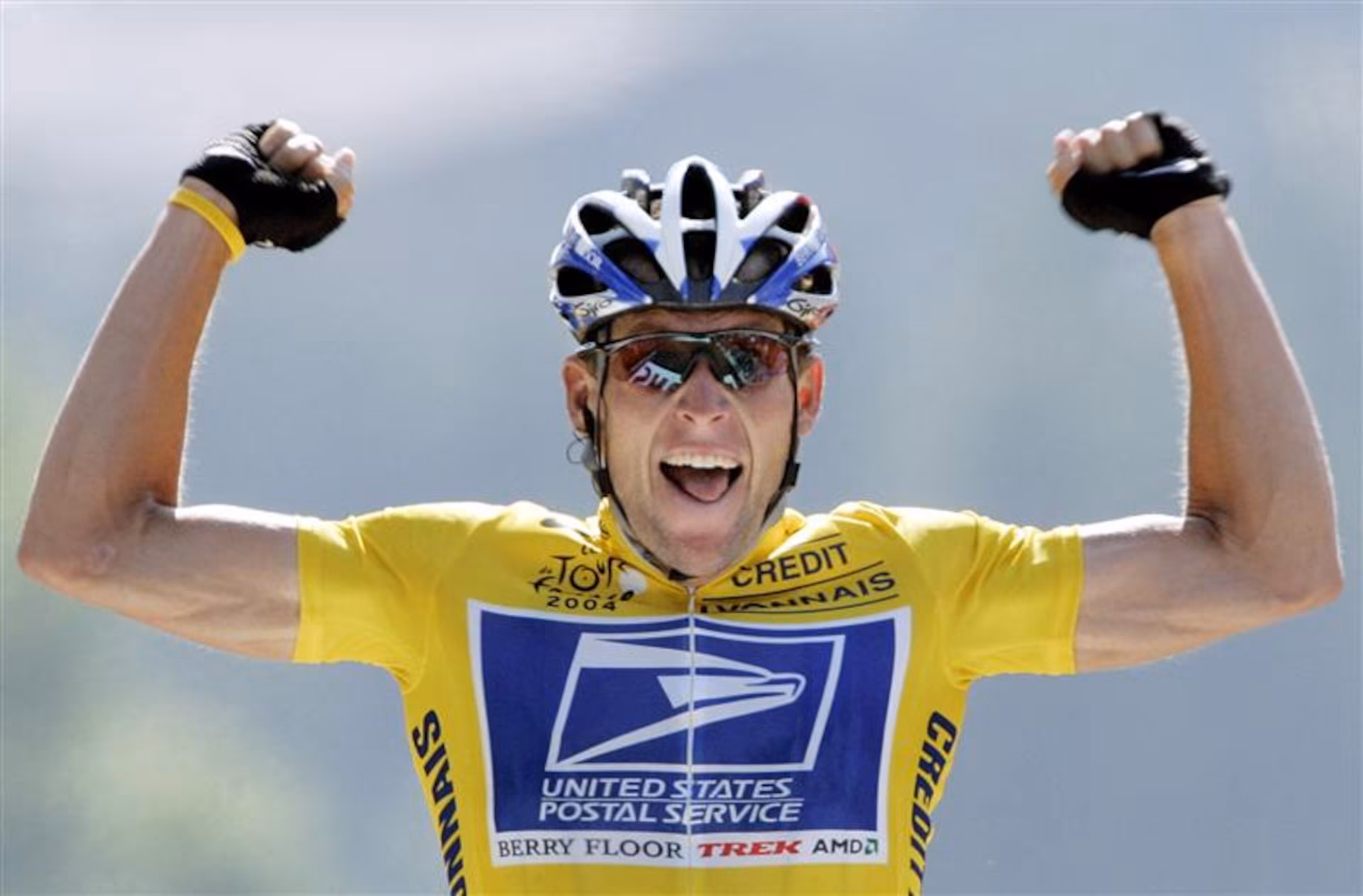 Lance Armstrong with arms raised triumphantly in celebration during a cycling race.