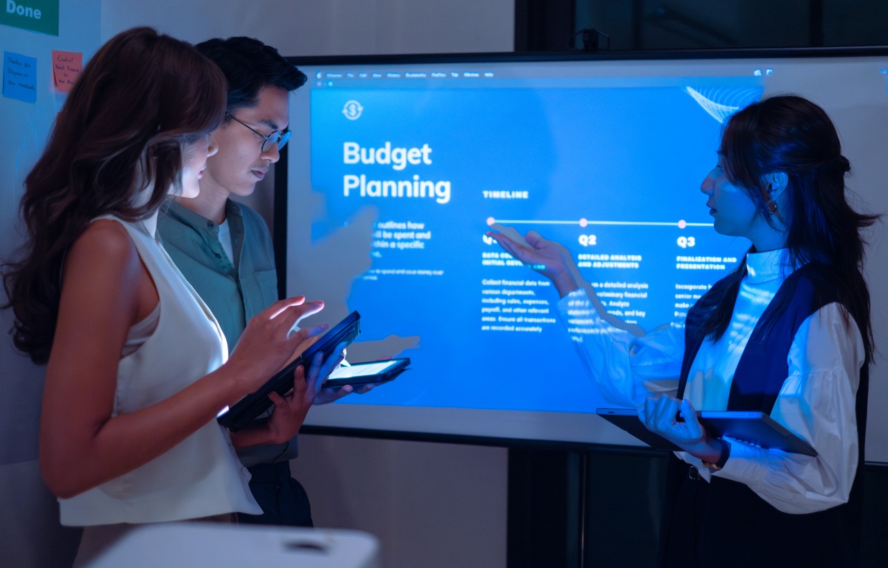 asian leader present business presentation in a dimly lit office, analyzing financial charts and data projections on a screen