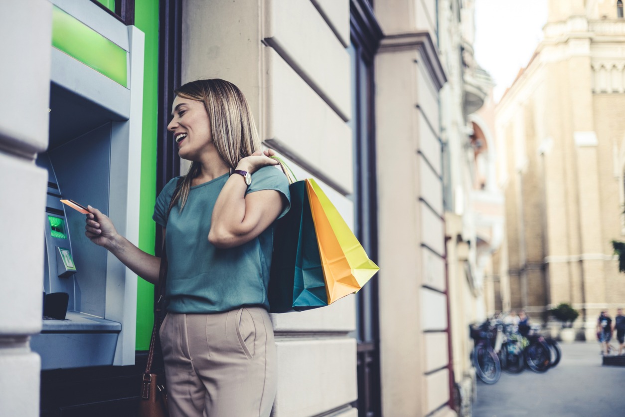 beautiful mature woman looking away in front of atm and shopping bags. purchases, black friday, discounts, sale concept.. young woman taking the money from the atm machine in the city.