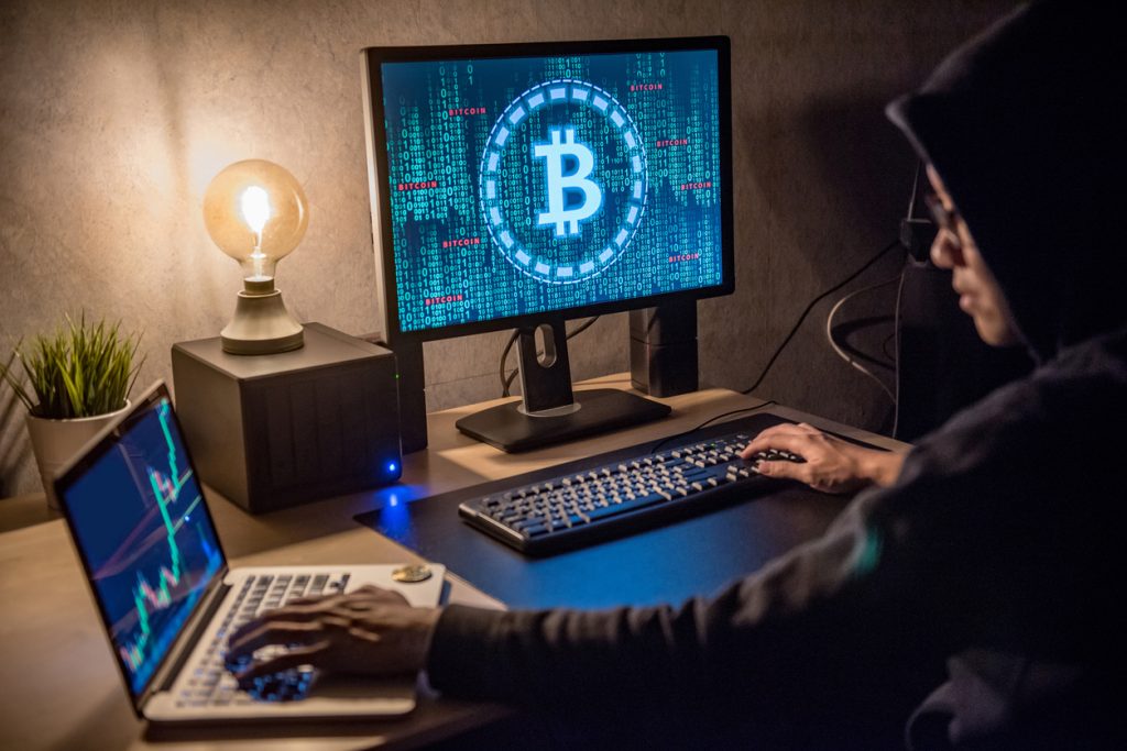 hacker man using laptop and computer with bitcoin green binary graphic and cryptocurrency candlestick graph price on monitor screen