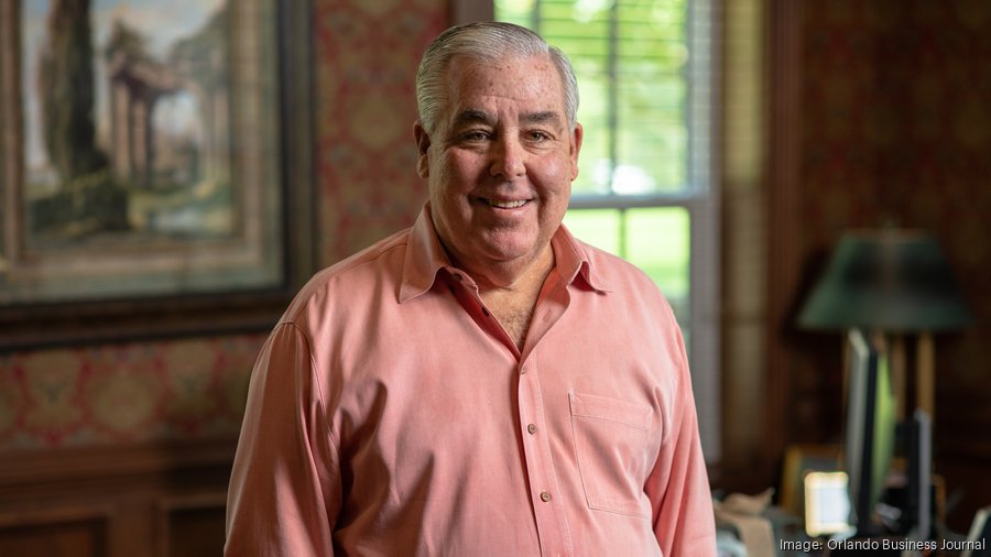 John Morgan smiling warmly while wearing a bright pink shirt.