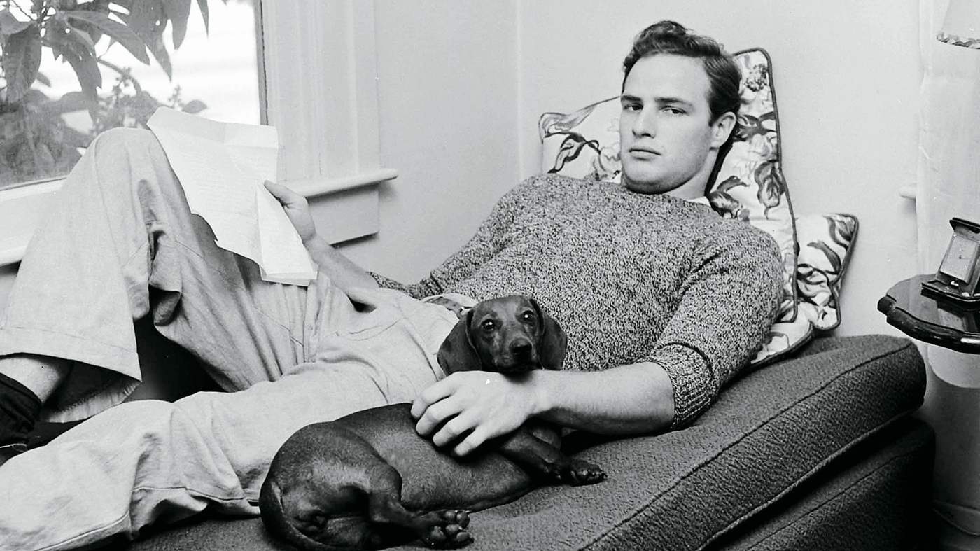 Marlon Brando lying down reading a script with his dog resting beside him.