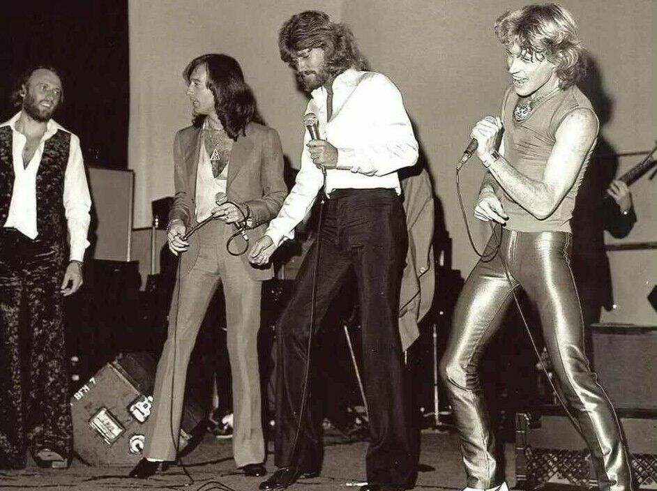 Andy Gibb performing on stage with his brothers Barry, Robin, and Maurice Gibb during a rare joint appearance.