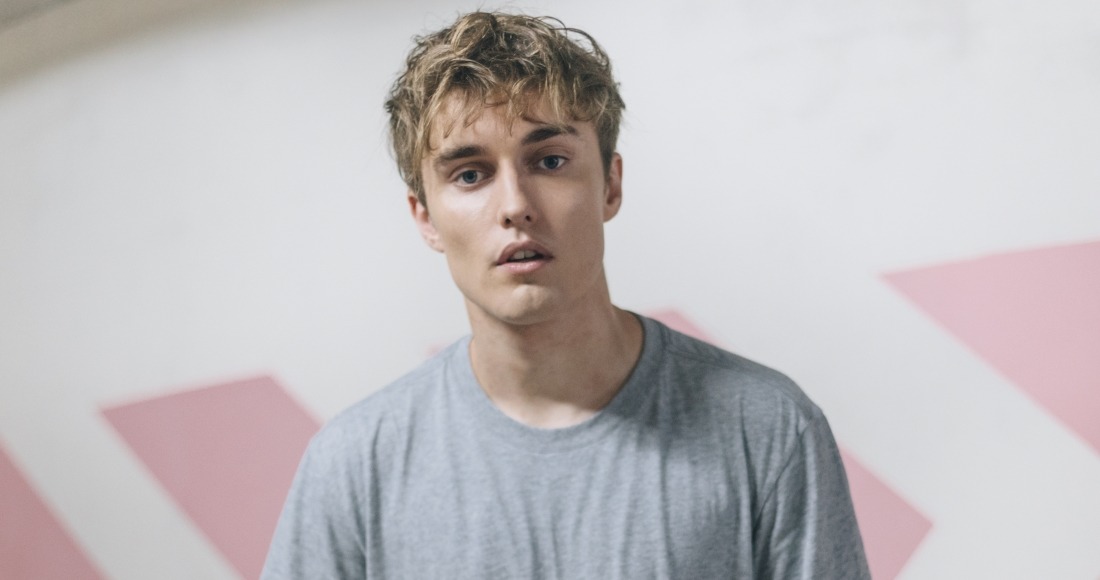 Young Sam Fender wearing a grey t-shirt, looking thoughtfully ahead.