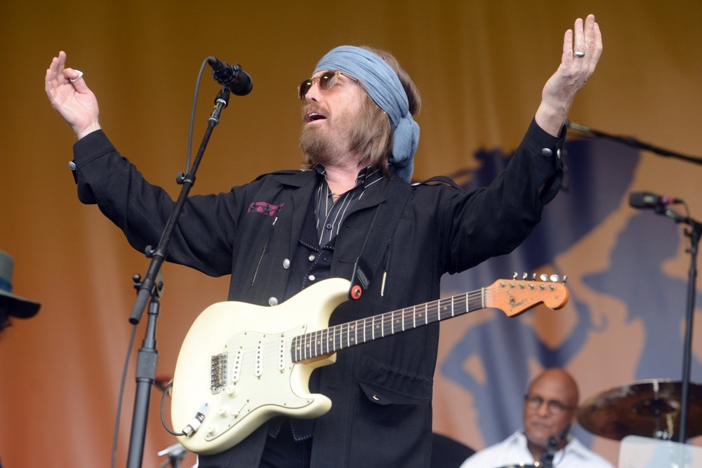 Tom Petty on stage with arms raised, energizing the crowd during a live concert performance.