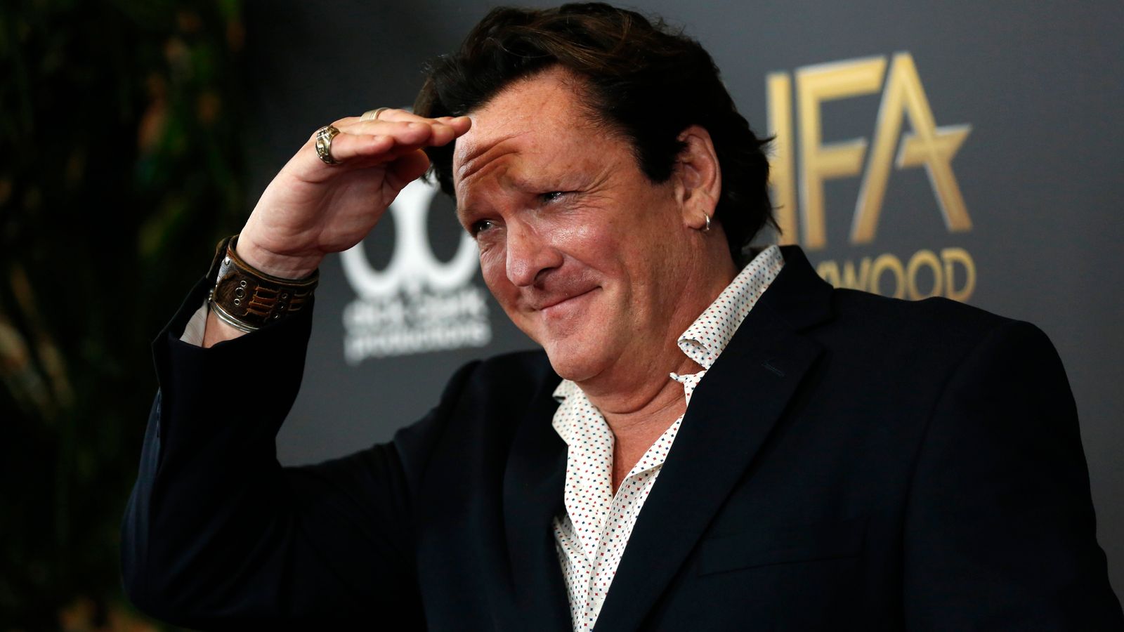 Michael Madsen smiles and shields his eyes on the red carpet at a Hollywood Film Awards event.